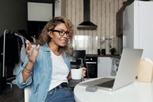 Woman with glasses on sitting in front of laptop with a cup of coffee, discussing mental health.